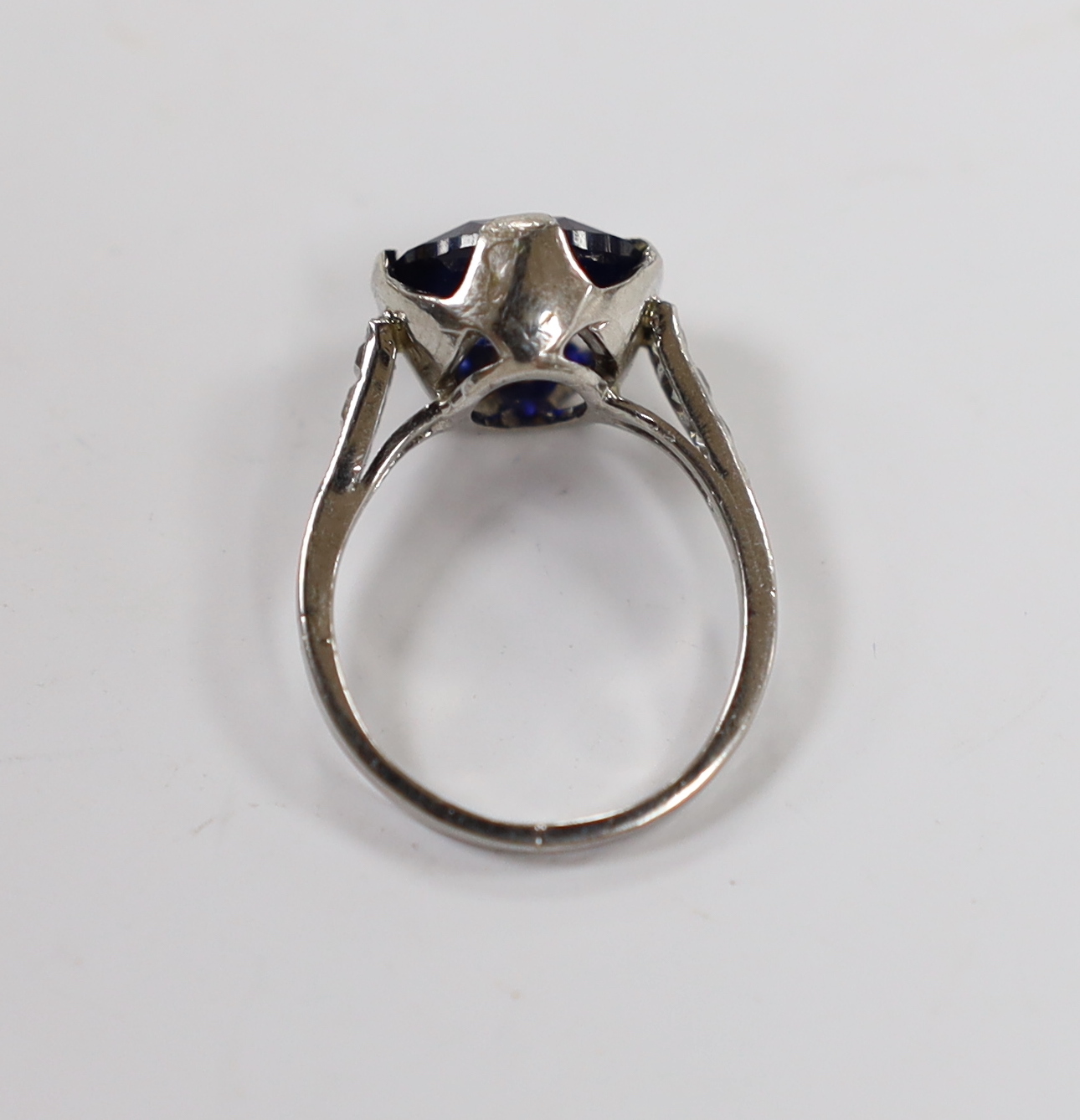 A plat. and iridium, single stone oval cut synthetic sapphire set ring, with graduated diamond chip set shoulders, the shank bearing the signature 'Tiffany & Co', size G, gross weight 3.7 grams.